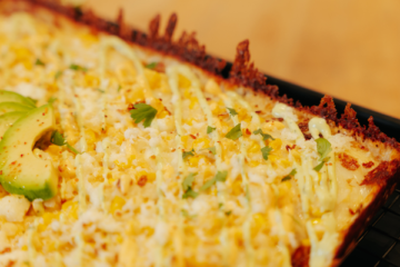 Golden-brown baked mac and cheese casserole with melted cheese topping and fresh herb garnish for food service distribution.