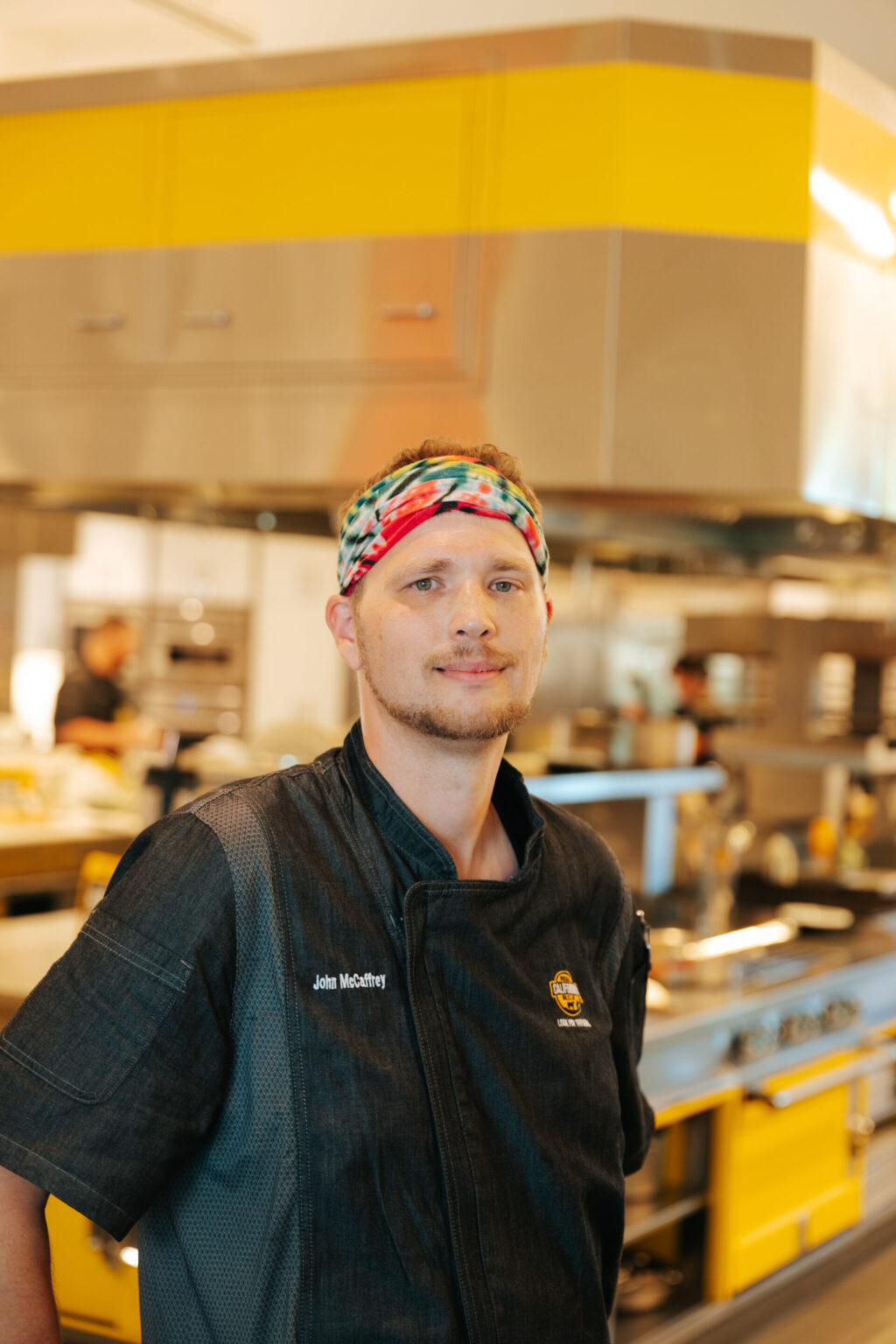 Professional food service worker wearing headband in modern commercial kitchen with yellow accents and equipment.