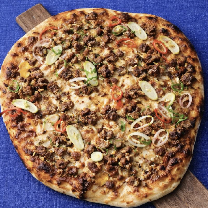 Premium ground beef pizza topped with melted cheese, sliced scallions, and red chili garnish, ideal for commercial foodservice and wholesale distribution.