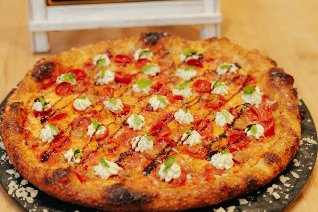 Professional gourmet pizza topped with fresh mozzarella dollops, red peppers, and green herbs on dark plate.