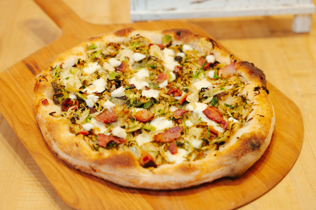 Artisanal pizza topped with chopped pistachios, crispy pancetta, fresh mozzarella, and herbs on a golden-baked crust.