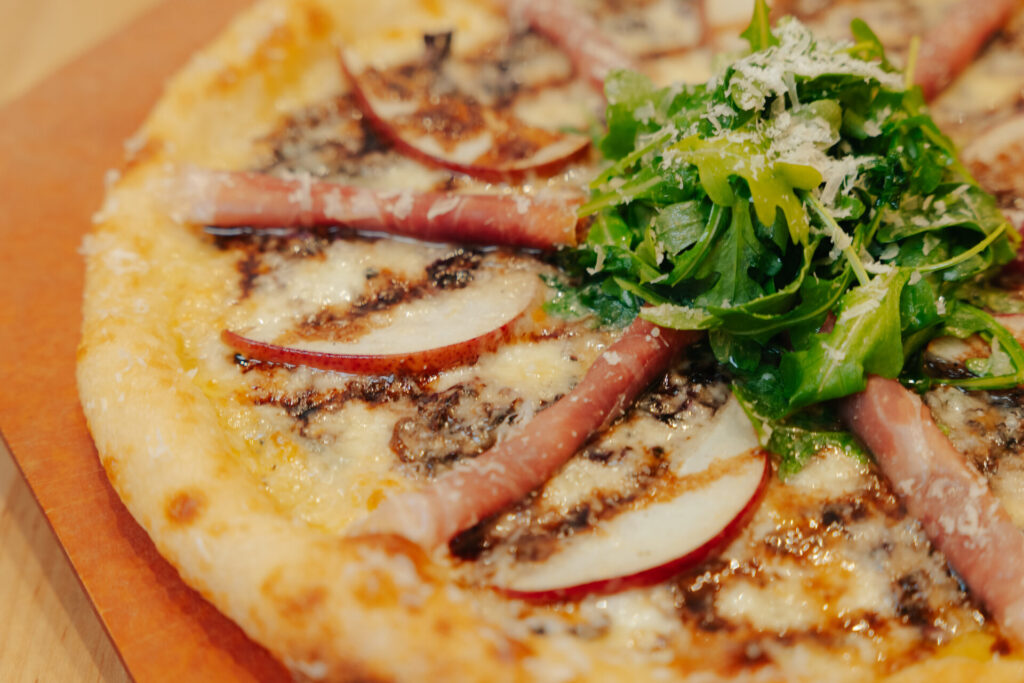 Artisan pizza slice topped with melted cheese, sliced apples, and fresh arugula garnish for upscale foodservice.