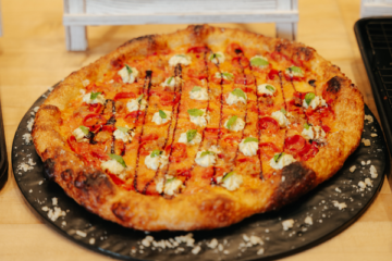 Artisanal pizza featuring tomato sauce, fresh mozzarella dollops, and basil garnish on a black pizza plate, ideal for wholesale food suppliers.