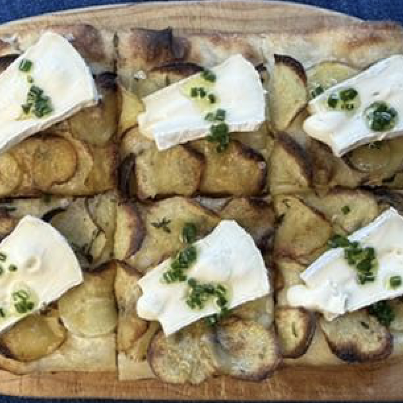 Professional food service platter featuring sliced potatoes topped with white cheese and fresh chives garnish, ideal for wholesale catering and food distribution.
