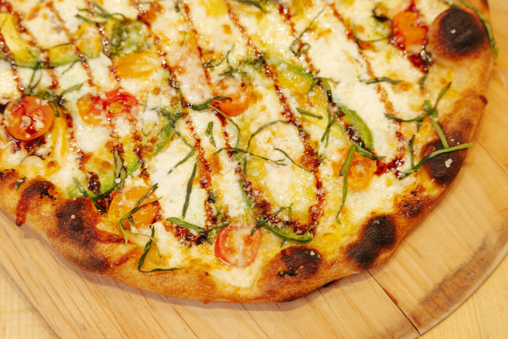 Artisan pizza topped with melted cheese, fresh vegetables, chives, and herbs on wooden serving board.