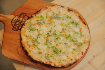 White pizza on wooden serving board topped with fresh green herbs and spices, ideal for foodservice distribution.