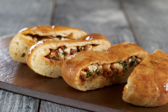Three pieces of golden-brown baked bread stuffed with a savory filling of chicken, herbs, and vegetables, displayed on a dark wooden board.