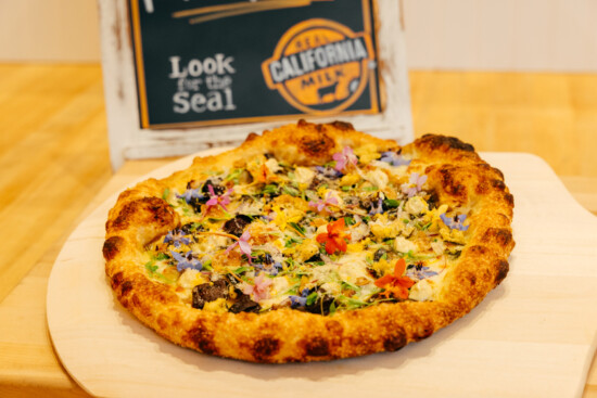 Artisan pizza featuring fresh toppings and Real California Milk on a rustic wooden board.