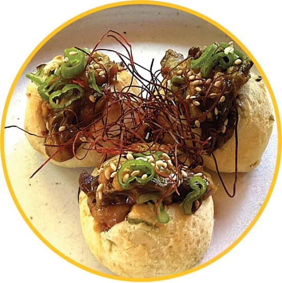 Gourmet bulgogi cheesesteak pao sandwich topped with melted cheese, microgreens, sesame seeds, and crispy fried onion strings for foodservice distribu