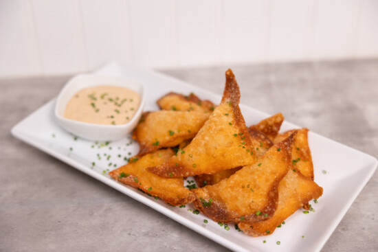 Crispy fried wontons served with a creamy dipping sauce and garnished with chives.