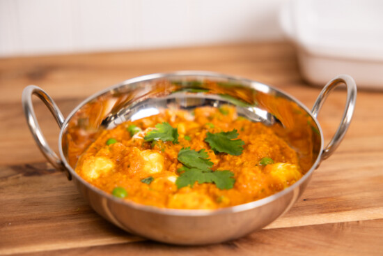 Vibrant curry paneer dish in a traditional bowl, garnished with cilantro and peas.