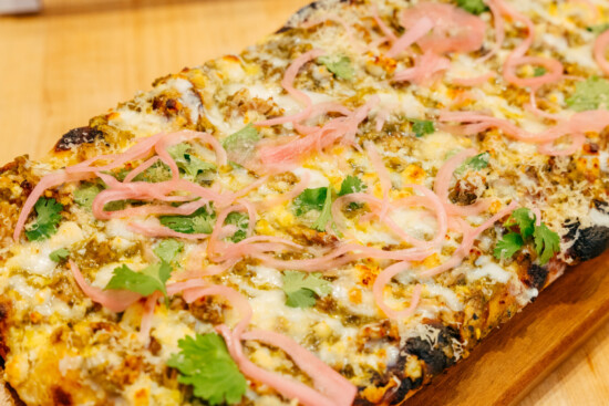 Mouthwatering flatbread with cheese, meat, and fresh garnishes on a wooden board.