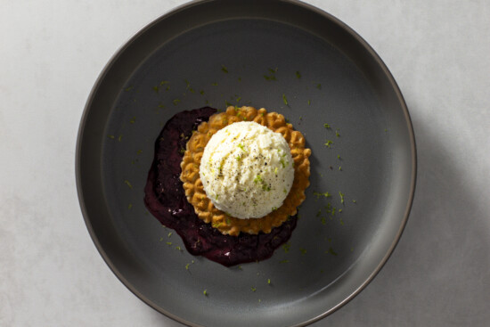 Elegant dessert featuring tart, creamy ice cream, berry sauce, and lime zest garnish.