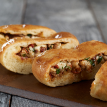 Three pieces of golden-brown baked bread stuffed with a savory filling of chicken, herbs, and vegetables, displayed on a dark wooden board.