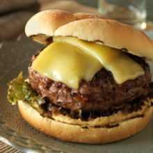 A close-up of a cheeseburger with melted yellow cheese, a thick beef patty, leafy lettuce, and a toasted bun, served on a plate.