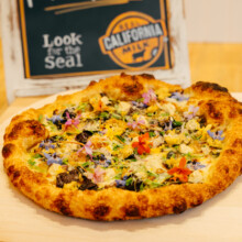Artisan pizza featuring fresh toppings and Real California Milk on a rustic wooden board.