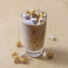 Iced caramel corn latte beverage topped with popcorn, chocolate shavings, and whipped cream garnish for food service applications.