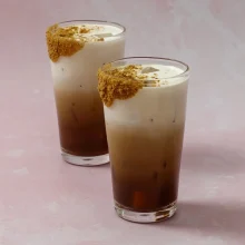 Two iced cheesecake lattes with layered espresso and cream, topped with cinnamon cookie garnish, ideal for foodservice and cafe wholesale distribution.