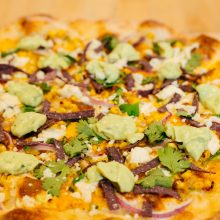 Vibrant pizza topped with guacamole, feta, corn, and colorful veggies, perfect for sharing.