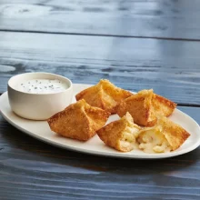 Golden-fried mac and cheese bites served with creamy dipping sauce on white plate for foodservice.