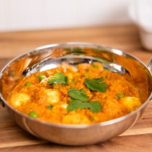 Vibrant curry paneer dish in a traditional bowl, garnished with cilantro and peas.
