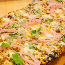 Mouthwatering flatbread with cheese, meat, and fresh garnishes on a wooden board.