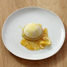 Elegant lemon dessert with creamy mousse, citrus sauce, and lemon slices on a graham crust.
