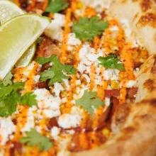 Grilled corn elote topped with crumbled queso fresco, chili powder, cilantro and lime wedge on charred tortilla.