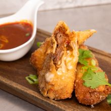 Golden-fried dumplings served with a vibrant dipping sauce and fresh green garnishes.