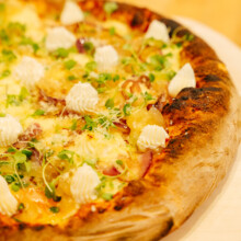 Gourmet pizza with creamy cheese and microgreens on a rustic wooden board.