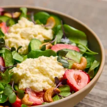 Fresh strawberry and Persian cucumber salad with microgreens and edible flowers in a modern serving bowl for wholesale food service.