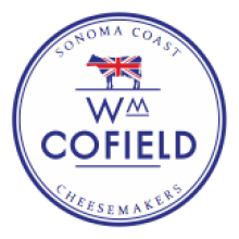 Circular logo for WM Cofield Cheesemakers. Features a cow with a British flag pattern and text reading “Sonoma Coast Cheesemakers” and “WM Cofield” in blue capital letters.