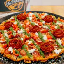 Gourmet pizza with vibrant toppings, artistic rose garnishes, and fresh pesto for culinary appeal.