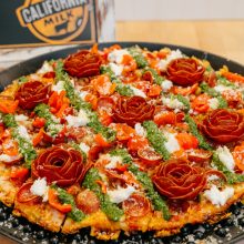 Gourmet pizza with vibrant toppings, artistic rose garnishes, and fresh pesto for culinary appeal.