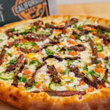 Delicious pizza topped with marinated steak, vibrant vegetables, and fresh cheese on a rustic board.