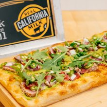 Delicious rectangular pizza topped with avocado, seared meat, arugula, and jalapeños.
