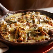 A sizzling skillet filled with melted cheese, browned ground meat, and strips of green peppers, creating a hot and savory dish. Steam rises from the surface, indicating it is freshly cooked.