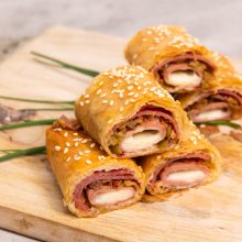 Savory rolled pastries filled with ham and cheese on a wooden cutting board.
