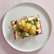 Vibrant gourmet dish with arugula, radishes, olives, and golden protein skewers on a colorful base.