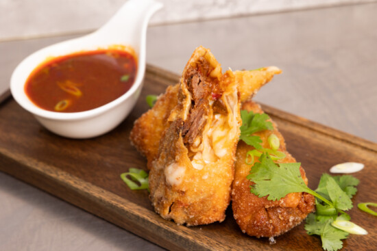 Golden-fried dumplings served with a vibrant dipping sauce and fresh green garnishes.