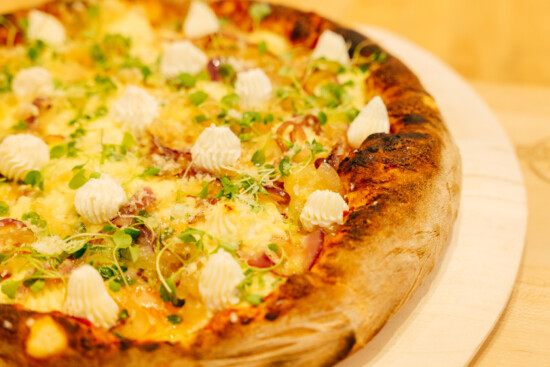 Gourmet pizza with creamy cheese and microgreens on a rustic wooden board.