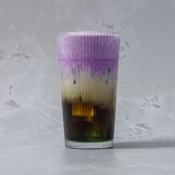 Vibrant layered pandan ube latte with purple, cream, and dark espresso layers in a ribbed glass, ideal for specialty beverage foodservice suppliers.