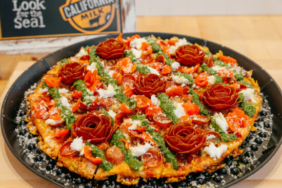 Gourmet pizza with vibrant toppings, artistic rose garnishes, and fresh pesto for culinary appeal.