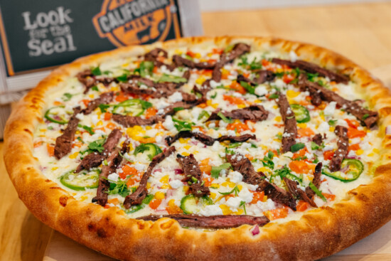 Delicious pizza topped with marinated steak, vibrant vegetables, and fresh cheese on a rustic board.
