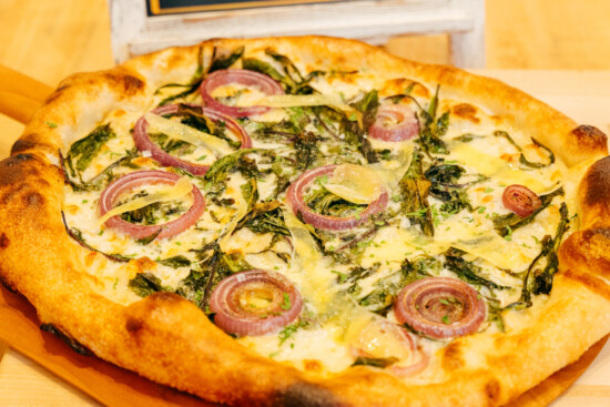 Artisan pizza topped with sautéed greens, cheese, and red onion on a golden-brown crust.