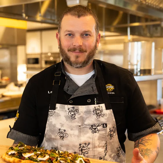 Professional chef in commercial kitchen displays freshly prepared gourmet pizza, exemplifying quality food service and culinary expertise for wholesal