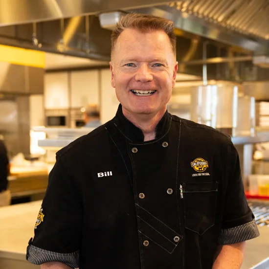 Bill, a smiling foodservice industry ambassador wearing black chef coat in modern commercial kitchen setting.