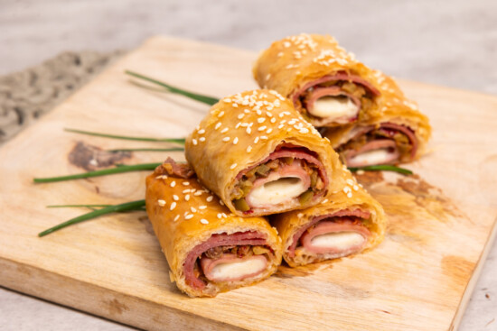 Savory rolled pastries filled with ham and cheese on a wooden cutting board.